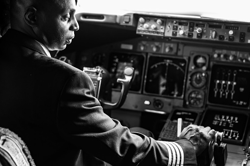 Rear view of a male pilot adjusting switches on the control panel while sitting inside cockpit. Man operating the switches while flying a modern airplane jet.