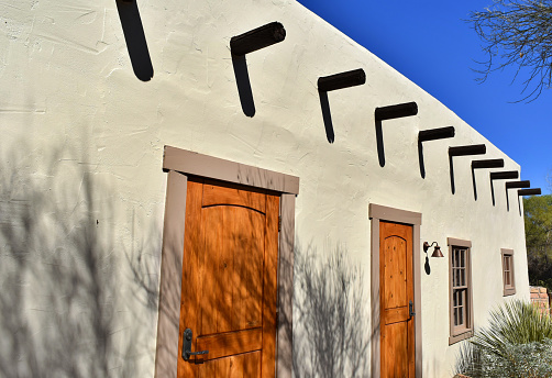 A light adobe building with bright orange doors contrasts against a deep blue sky.