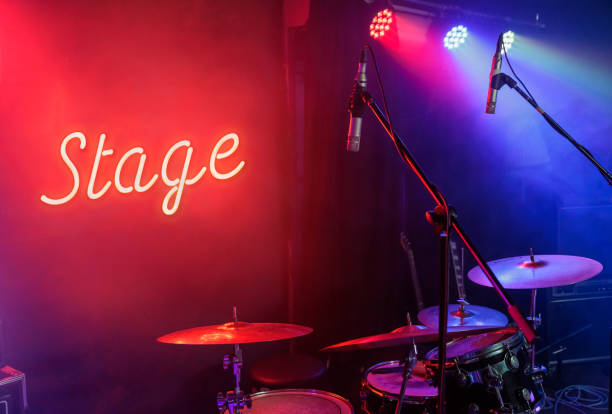 stage text glowing neon on a wall behind a drum set illuminated by stage lights ready to record and play music stock photo