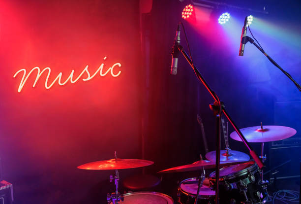 glowing neon on a wall behind a drum set illuminated by stage lights ready to record and play music