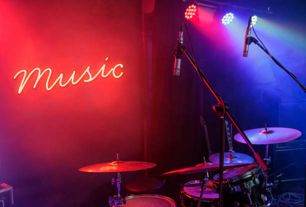 music text glowing neon on a wall behind a drum set illuminated by stage lights ready to record and play music stock photo