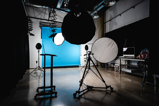 Interior of modern spacious photo studio with hanging blue background spotlight and laptop before shooting