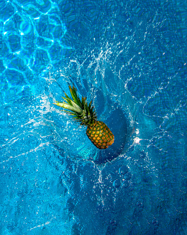 A fresh pineapple fruit falls on the water