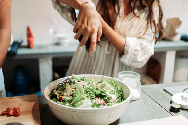main féminine versant de l’huile d’olive sur la salade de légumes frais - cuisine méditerranéenne photos et images de collection