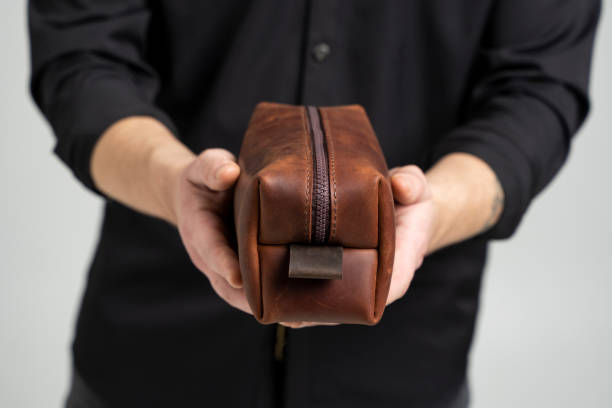Man's brown leather personal cosmetic bag or pouch for toiletry accessory in a men's hands in black shirt. Style, retro, fashion, vintage and elegance. stock photo
