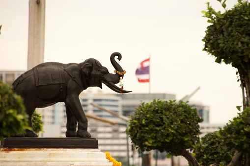 A statue of an elephant with a blurred Thai flag on the background