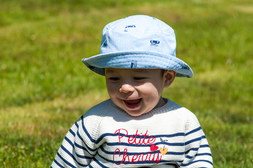 A closeup shot of a cute happy little boy in a hat sitting on a grass