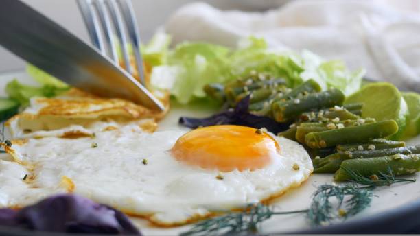 istock Breakfast with scrambled eggs, a knife and fork cut fried eggs for eating protein and healthy fats for breakfast, fried eggs with vegetables help you get enough for the whole day, for productive work. 1441188490