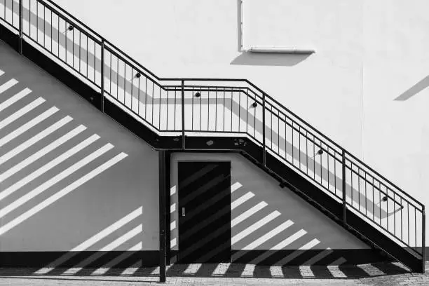 An outside staircase runs diagonally along the house wall and casts shadows on the wall and the paved floor - in black and white.