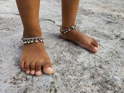 A closeup shot of brown child's feet with anklets on a beach
