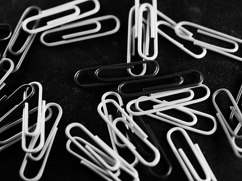 A grayscale shot of a pile of scattered paperclips on a black table