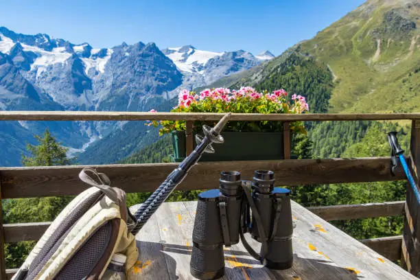 backpack with trekking poles and binoculars to enjoy panoramic view to Ortles Mountain range from Furkelhütte, Trafoi, Italy; alpine healthy lifestyle concept