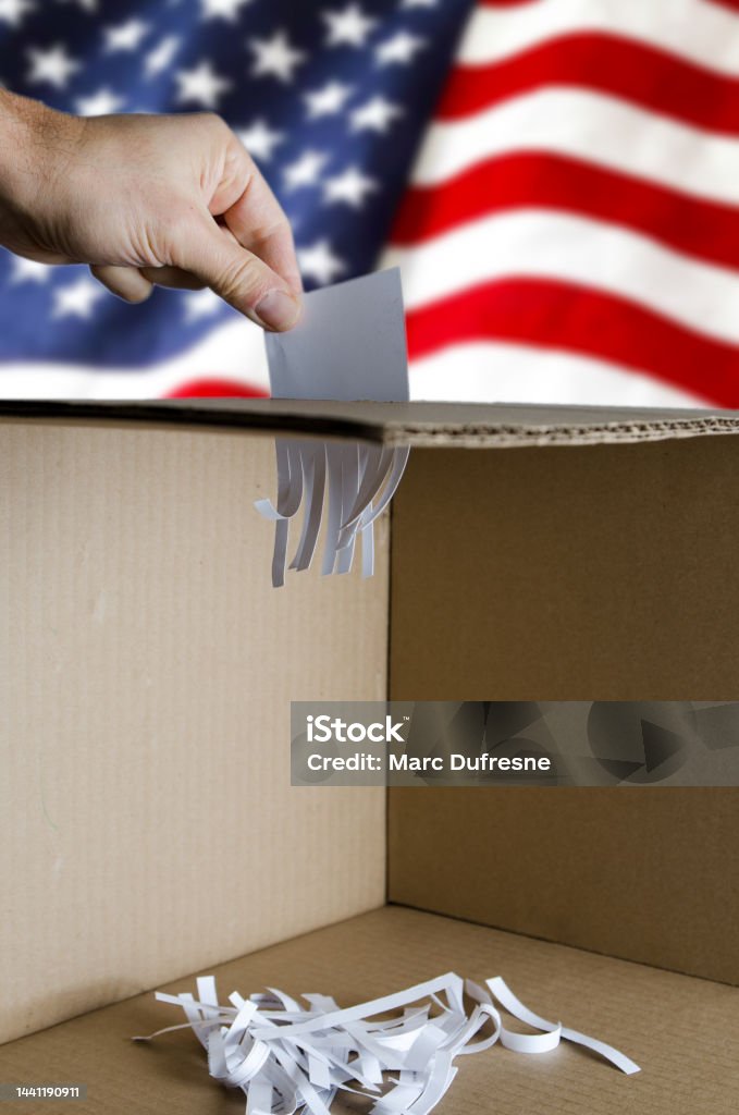 USA voting card being shredded when inserted in ballot box USA voting card being shredded when inserted in ballot box on USA flag background. Shredded paper at the bottom of the box. Adults Only Stock Photo