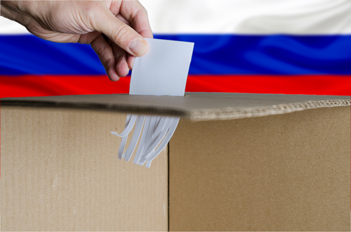 Voting card being shredded when inserted in ballot box on Russian flag background. Shredded paper at the bottom of the box.