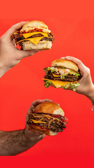 A vertical shot of three male hands holding hamburgers on an isolated red background