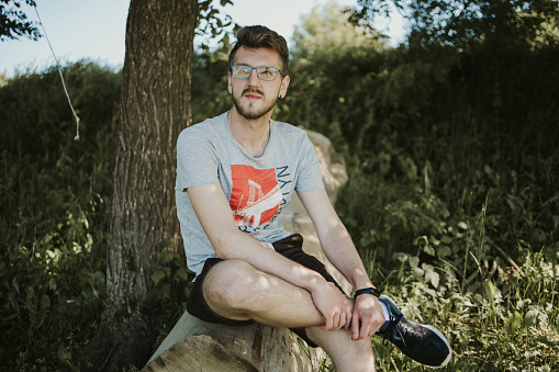 A Caucasian male sitting on a tree slog