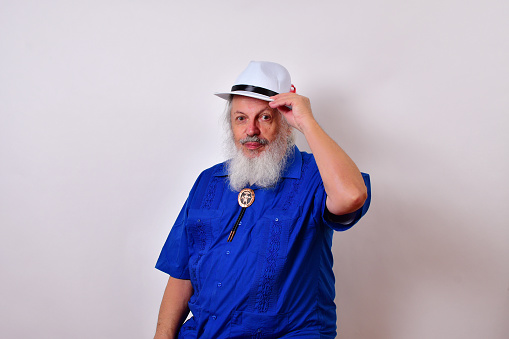 A respectful old man with a white fedora hat, blue guayabera shirt, and bolo tie tipping his hat