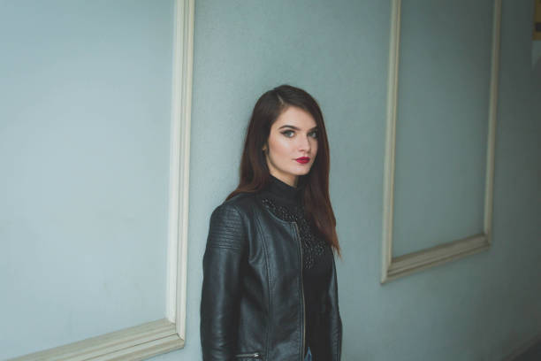 istock Young brunette female in a leather jacket posing in front of a wal 1441194865