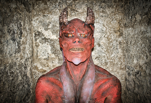 A red horned face demon on a concrete wall