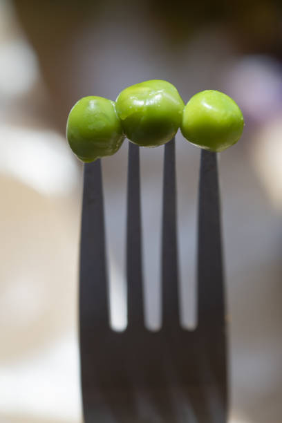 One circular wooden bowl full of delicious tasty juicy tempting bowl full of raw green peas in a bowl in  hand against a green colored lush horizontal background with depth of field .