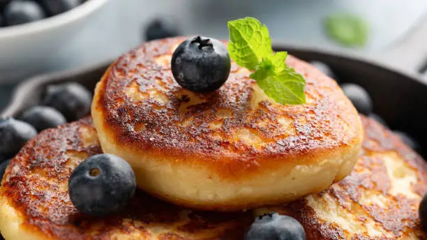 Cottage cheese pancakes served in cast iron frying pan with blueberries and mint leaves. Healthy breakfast food