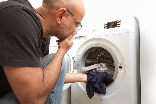 A male loading the washing machine with dirty clothes