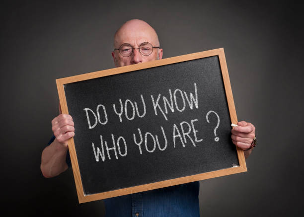 Do you know who you are? White chalk handwriting on a blackboard held by a senior man, teacher, mentor or presenter. Self awareness and personal development concept.