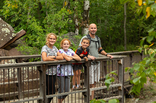 Father and three children smiling at the camera while standing on a bridge in the woods.