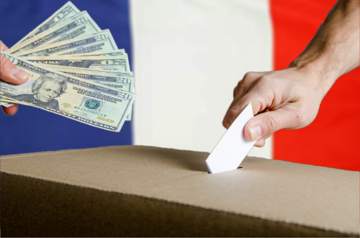 US Dollars handed to someone while putting his voting card in ballot box on French flag background.