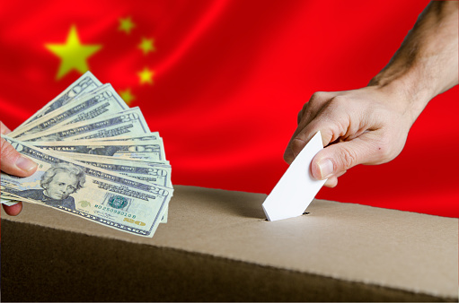 US Dollars handed to someone while putting his voting card in ballot box on Chinese flag background.