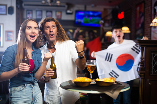 Group of happy friends with flag of South Korea celebrating victory of their favorite team in a beer bar