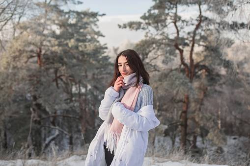 Brunette woman in white jacket and scarf in winter forest. Pretty woman enjoying vacation. Girl in nature. Feel happiness. Hoarfrost and snow on trees