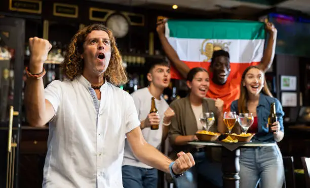 Photo of Emotional adult football fan cheering for favorite Iranian team in sports bar