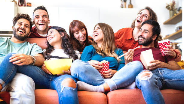 giovani amici che si divertono davvero insieme a casa guardando film su smart tv - concetto di stile di vita accogliente con persone felici che si rilassano sul divano del divano mangiando popcorn e cibo da asporto - filtro luminoso e vivido - italian culture women looking at camera cheerful foto e immagini stock