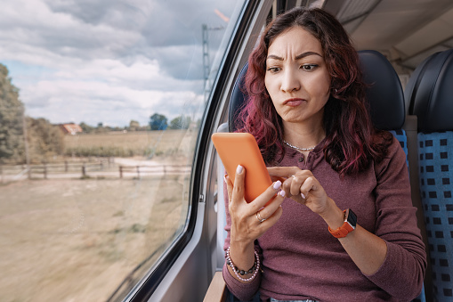 Annoyed girl unsuccessfully tries to catch a cellular signal or an unstable WiFi, holding her smartphone in her hands in train