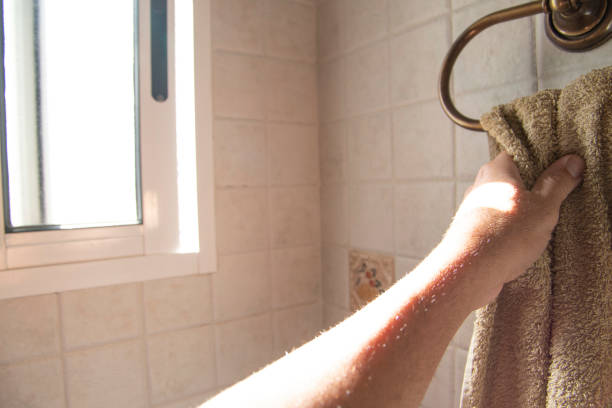 A hand picking up a hanging towel, in the bathroom passing the sun's rays through the window.