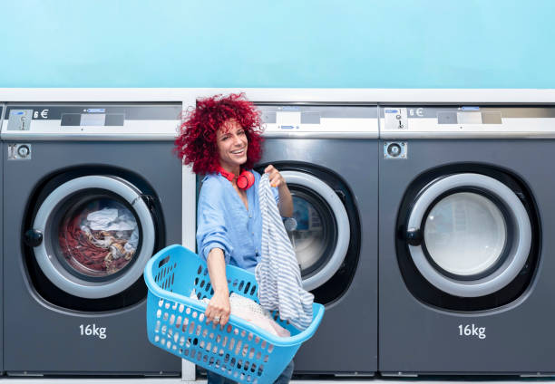 istock A smiling young woman with red afro hair doing laundry in a blue automatic laundromat 1441216057