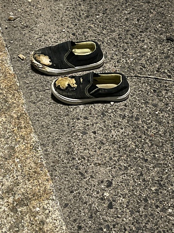 Vertical shot of damaged child's shoes abandoned on the road