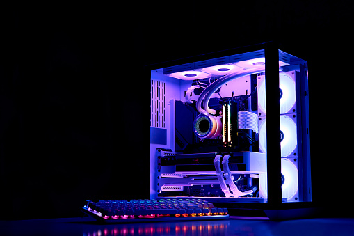 Gaming PC with rainbow LED light. Liquid cooled computer. Powerful PC in a glass case with keyboard. Gamer's workplace in a dark room, neon light.