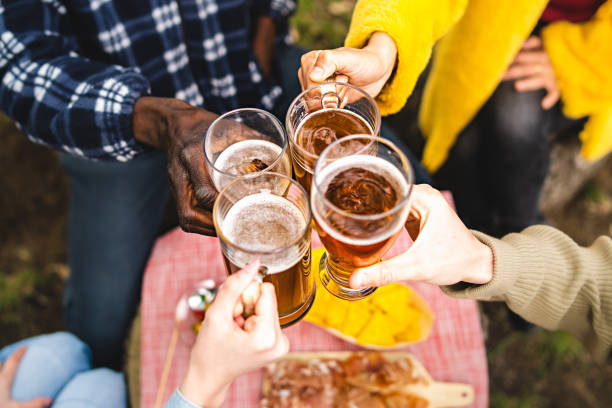 Closeup of multiethnic hands holding beer mugs and toasting together outdoors - Concept of multiracial young people gathering for happy hour drinking - main focus on the hand of the woman in yellow stock photo