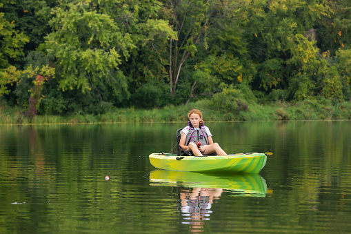 Young girl fishing from her green and yellow kayak.