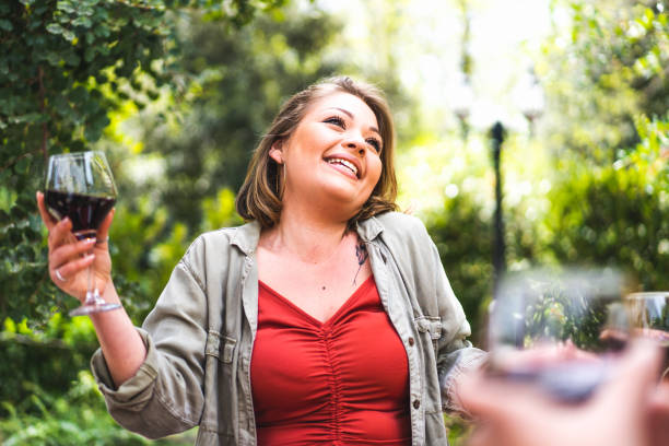 Happy young woman with a glass of red wine - portrait of a positive curvy girl holding a wineglass and enjoying life in the countryside - people lifestyle concept stock photo