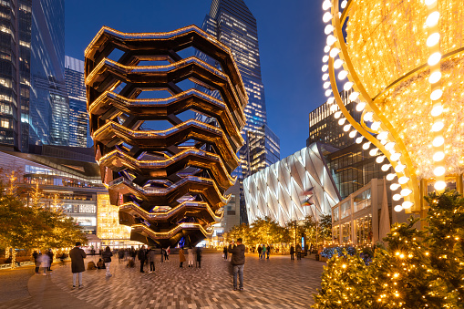 New York City, NY, USA - December 3, 2021: Hudson Yards esplanade with The Vessel (staircase) and the Shed in evening with Christmas decorations. Winter in Midtown West, Manhattan