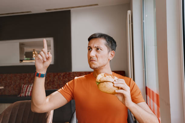 The annoyed and frustrated Man gestures to the waiter in the restaurant. Stale and spoiled food or wrong order. Frowned disgruntled man customer of a fast food restaurant digs into a burger and found a spoiled product in his lunch brat burger stock pictures, royalty-free photos & images