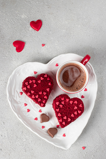 Cakes Red velvet in the shape of hearts on white plate and cup of coffee for Valentines Day, vertical image
