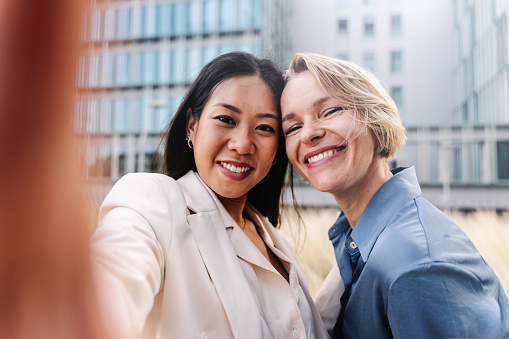 Happy Business women coworkers sharing selfie social media video call with professional colleague friend using on smartphone after work