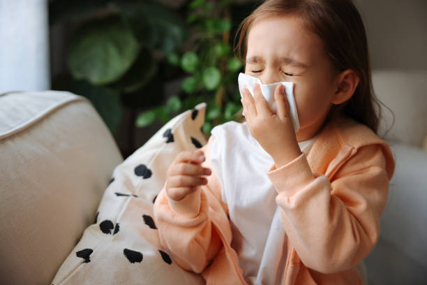 Little girl gets cold and blows her nose at home. Sick little schoolgirl coughs and blows nose wiping with white paper napkin. girl patient stock pictures, royalty-free photos & images