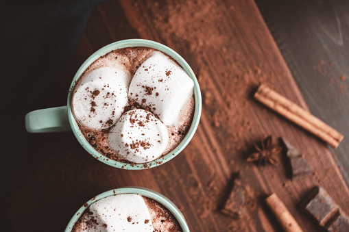 Hot chocolate drink with marshmallow in a cup on wooden board with cinnamon and star anise, top view.