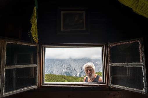 Open window of mountain bivouac, senior men looking inside from the window. Triglav national park, Julian Alps