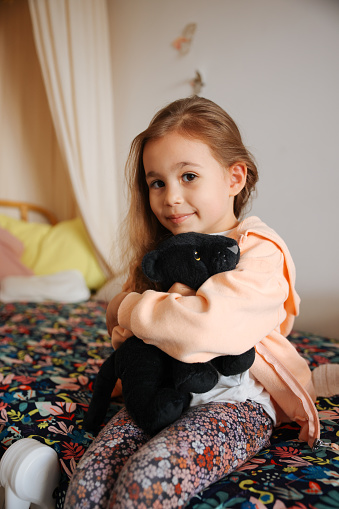 Adorable little girl is laughter in the bed. Portrait of content girl lying on bed with hands on chin, looking at camera.